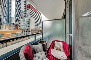 A balcony with a view of tall buildings, a wicker chair, a cushion, and a red cloth. - 🌿|| Cozy+Stylish Suite ||🍄 PRIME Entertainment District @ Spadina & King West! (Toronto)