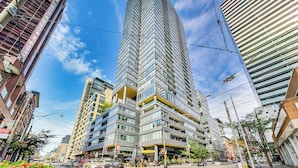 A modern high-rise building with a unique angular design, surrounded by other contemporary buildings. - 🌿|| Cozy+Stylish Suite ||🍄 PRIME Entertainment District @ Spadina & King West! (Toronto)