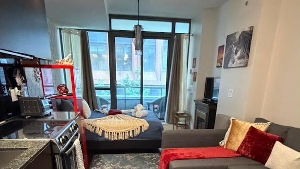 A modern living room with a sofa, a rug, and a kitchen area with a stove. - 🌿|| Cozy+Stylish Suite ||🍄 PRIME Entertainment District @ Spadina & King West! (Toronto)