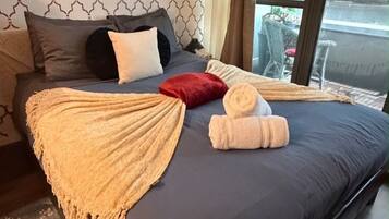 A neatly made bed with a blue mattress, a beige throw blanket, and a rolled-up towel.