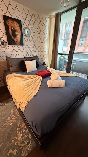 A neatly made bed with a blue mattress, a beige throw blanket, and a rolled-up towel.