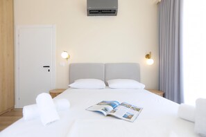 A hotel room with a bed, two bedside tables, a wall-mounted air conditioner, and two wall sconces.