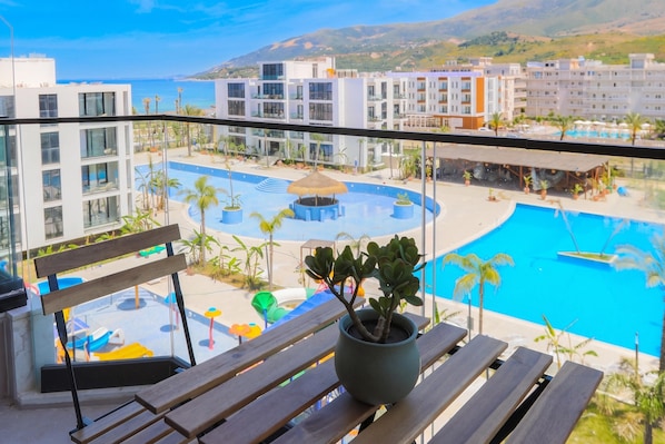 Un balcón con vistas a una piscina, palmeras y edificios modernos.