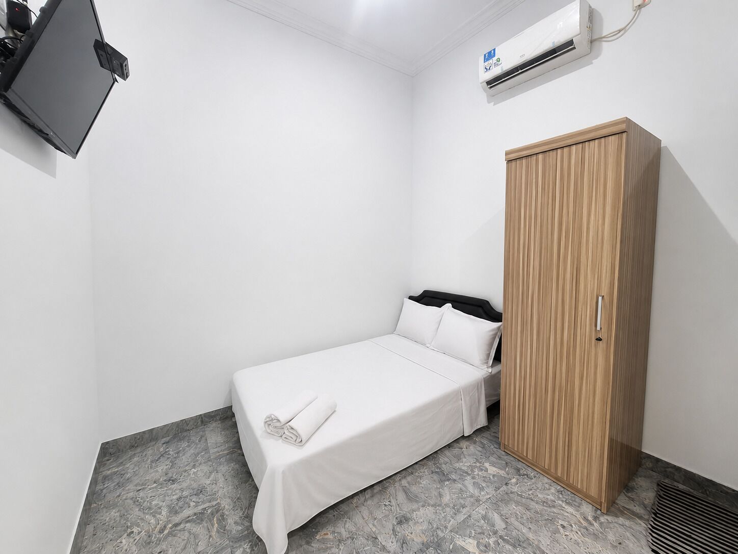 Un dormitorio pequeño y ordenado, con una cama individual, un armario de madera y un equipo de aire acondicionado instalado en la pared.