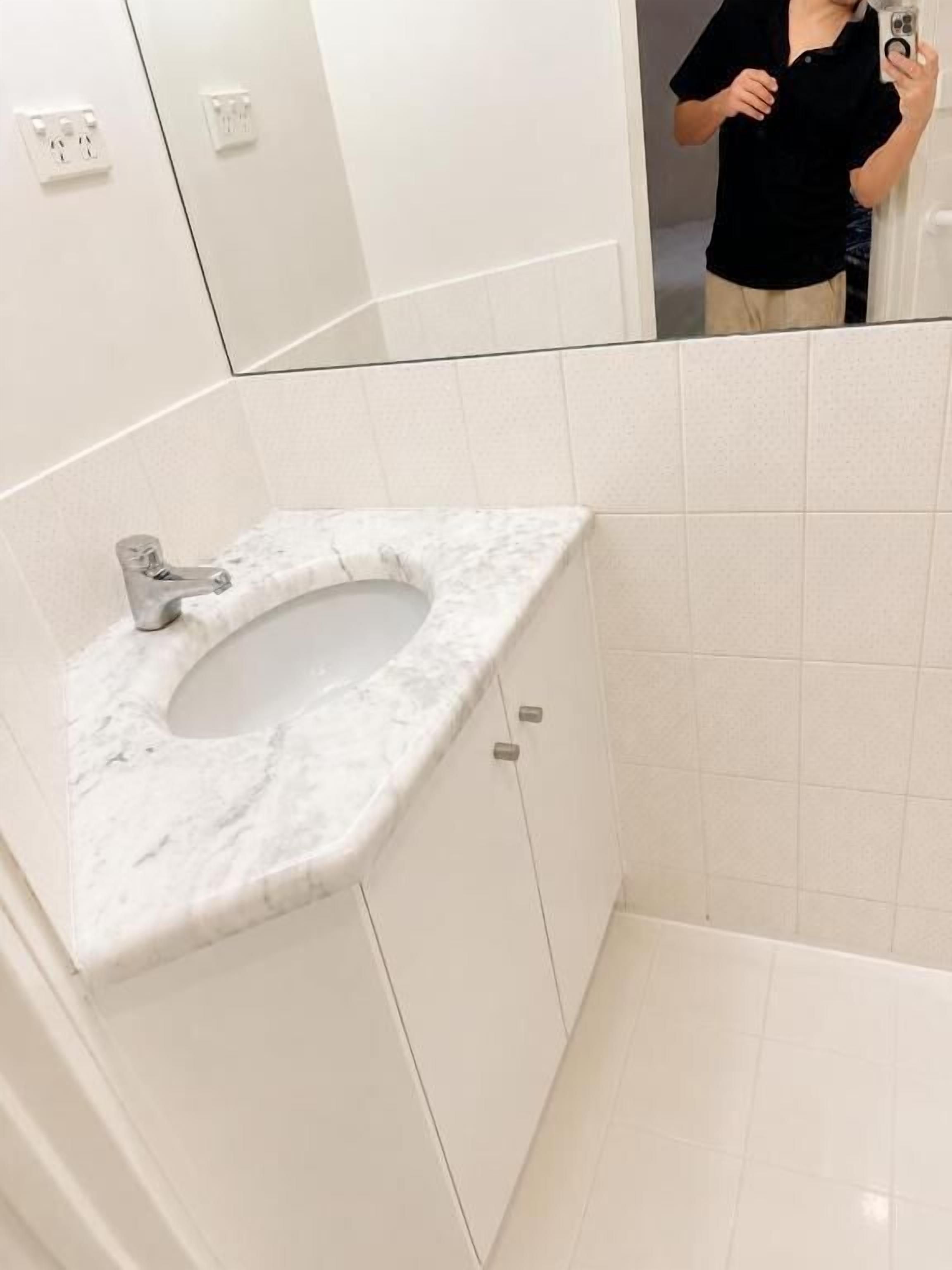 A bathroom with a marble sink, a mirror, and white tiled walls.