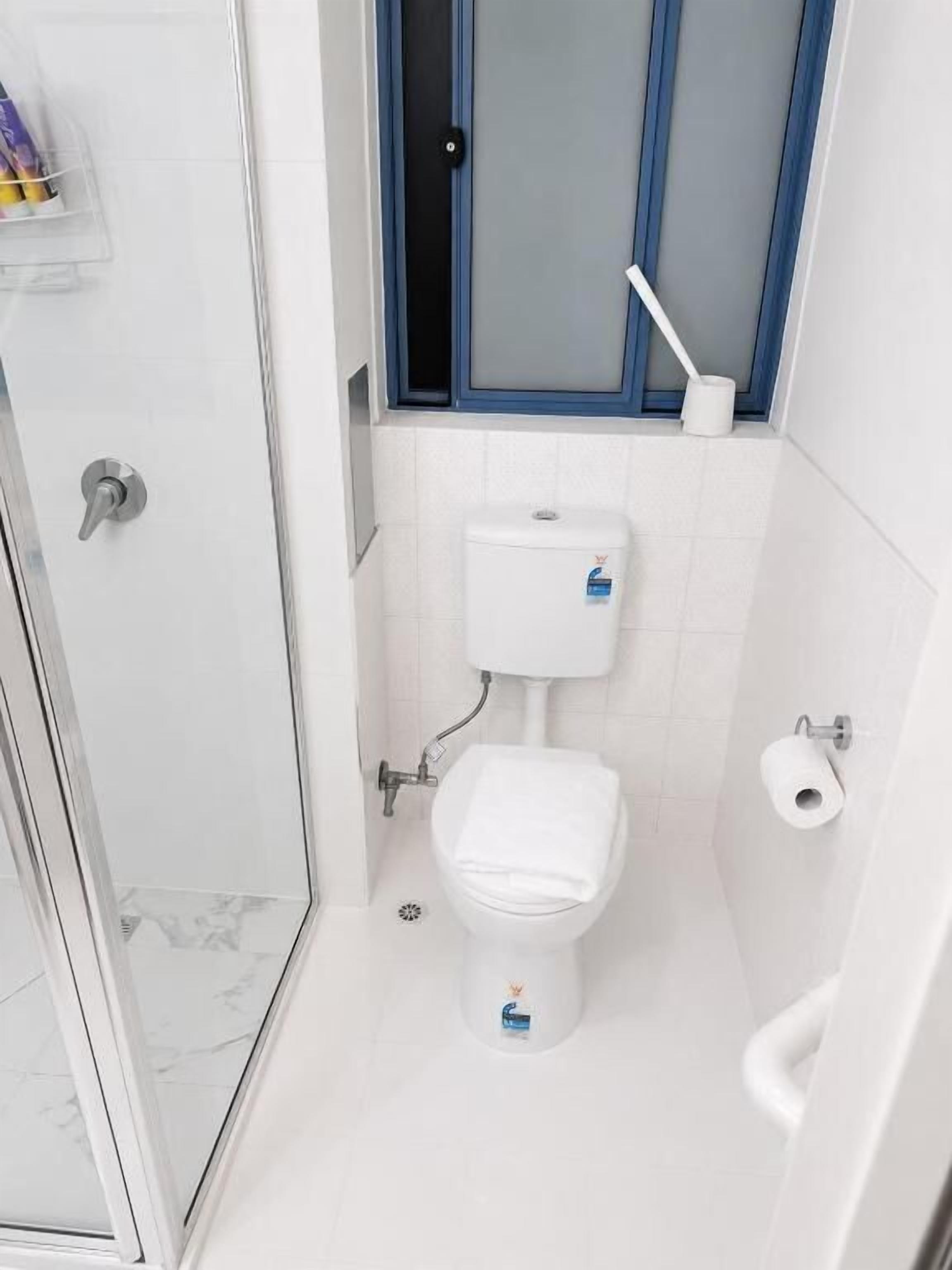 A small bathroom with a toilet, a shower, and a window.