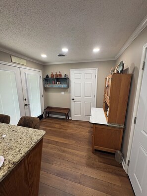 A kitchen with a granite countertop, wooden cabinets, a bench, and a door with a shelf above it.