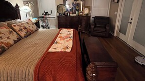 Een slaapkamer met een bed, een dressoir, een stoel, een bureau, een spiegel en een plafondventilator.
