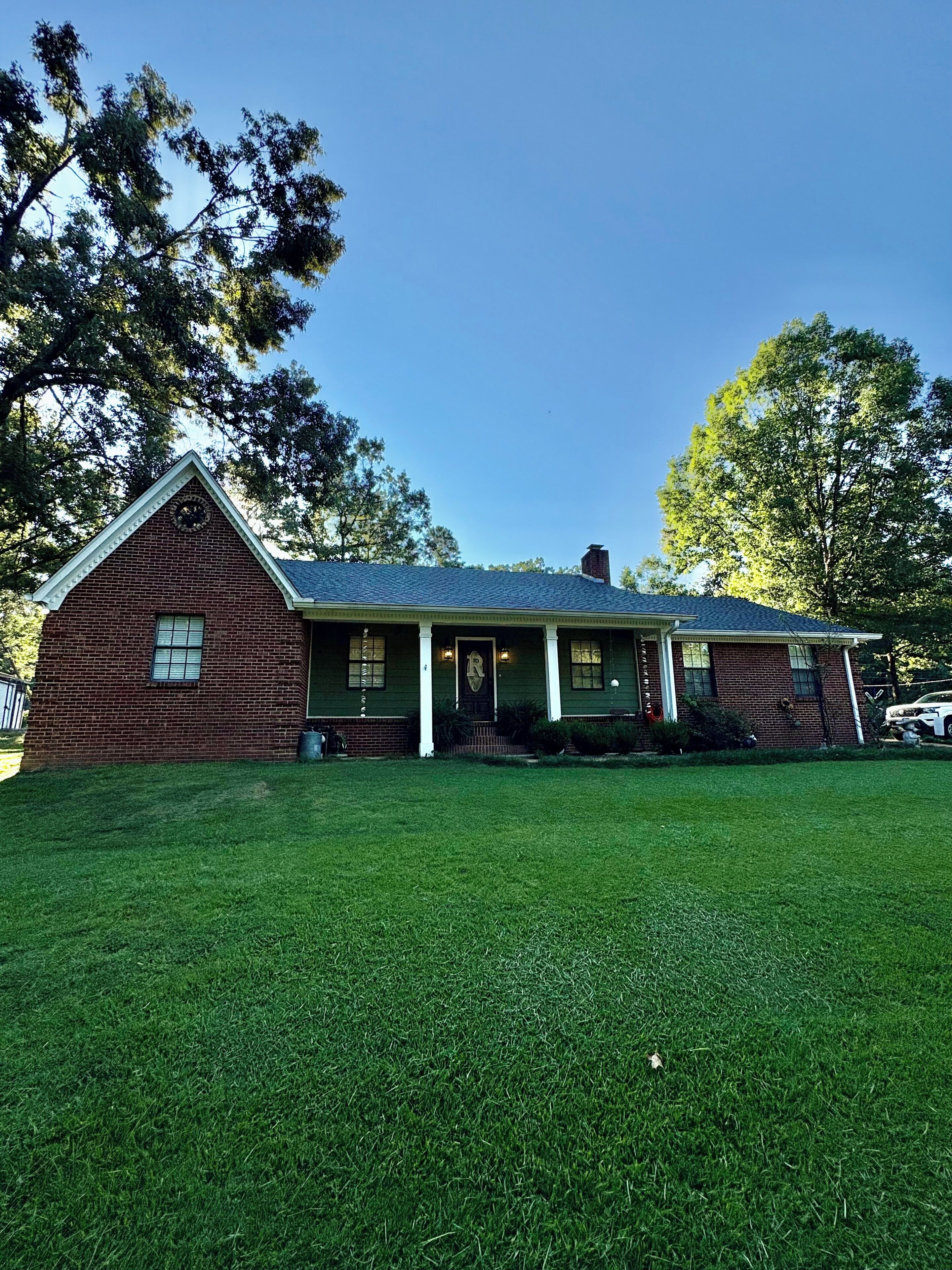 A two-story brick house with a front porch, a chimney, and a well-maintained lawn.