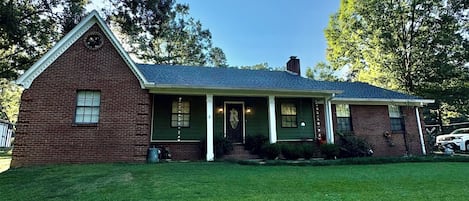 A two-story brick house with a front porch, a chimney, and a well-maintained lawn.
