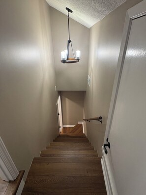 A staircase with wooden steps leading to a landing, a light fixture above, and a door on the right.