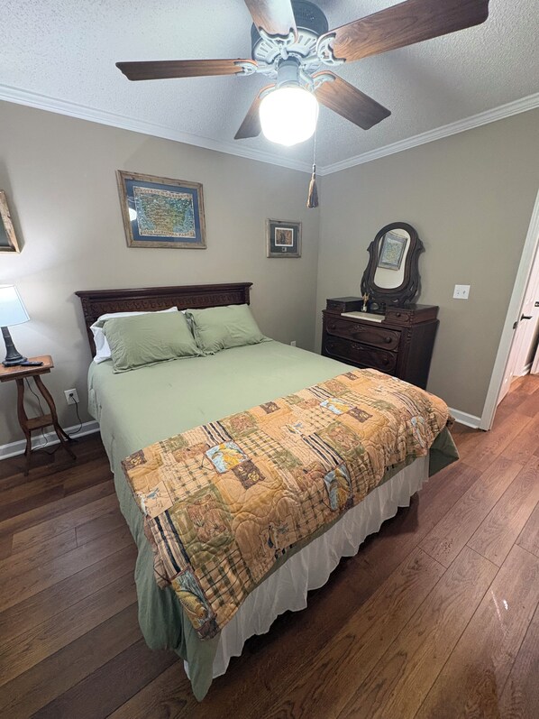 A bedroom with a bed, a ceiling fan, a dresser, and a nightstand.