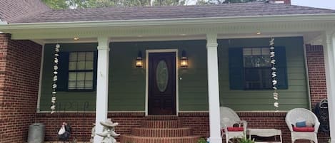 A brick house with a porch, two white wicker chairs, and a small garden.