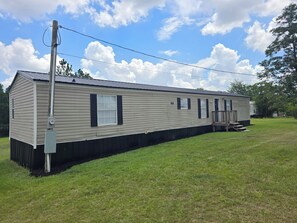 A single-story mobile home with a front porch, a utility pole, and a grassy yard.