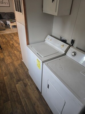 A laundry room with stacked washers and dryers, wooden flooring, and a white cabinet above the dryers.