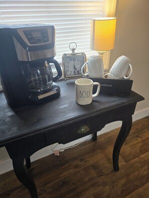 A coffee maker, a mug, a clock, and a lamp on a table.