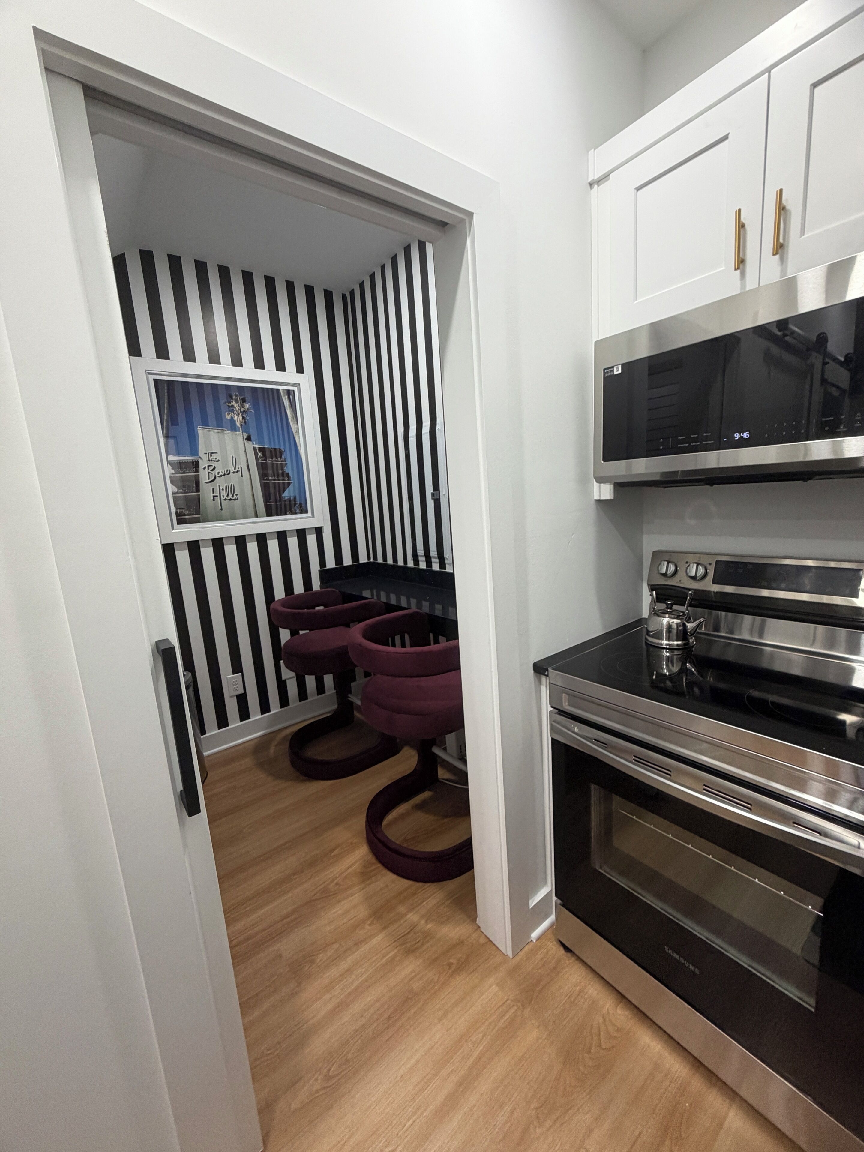 A kitchen with a microwave, oven, and a dining area with striped wallpaper and two chairs.