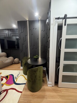 Ein modernes Interieur mit Essbereich, ausgestattet mit einem runden Tisch, grünen Sitzmöbeln und einem an der Wand montierten Fernseher.
