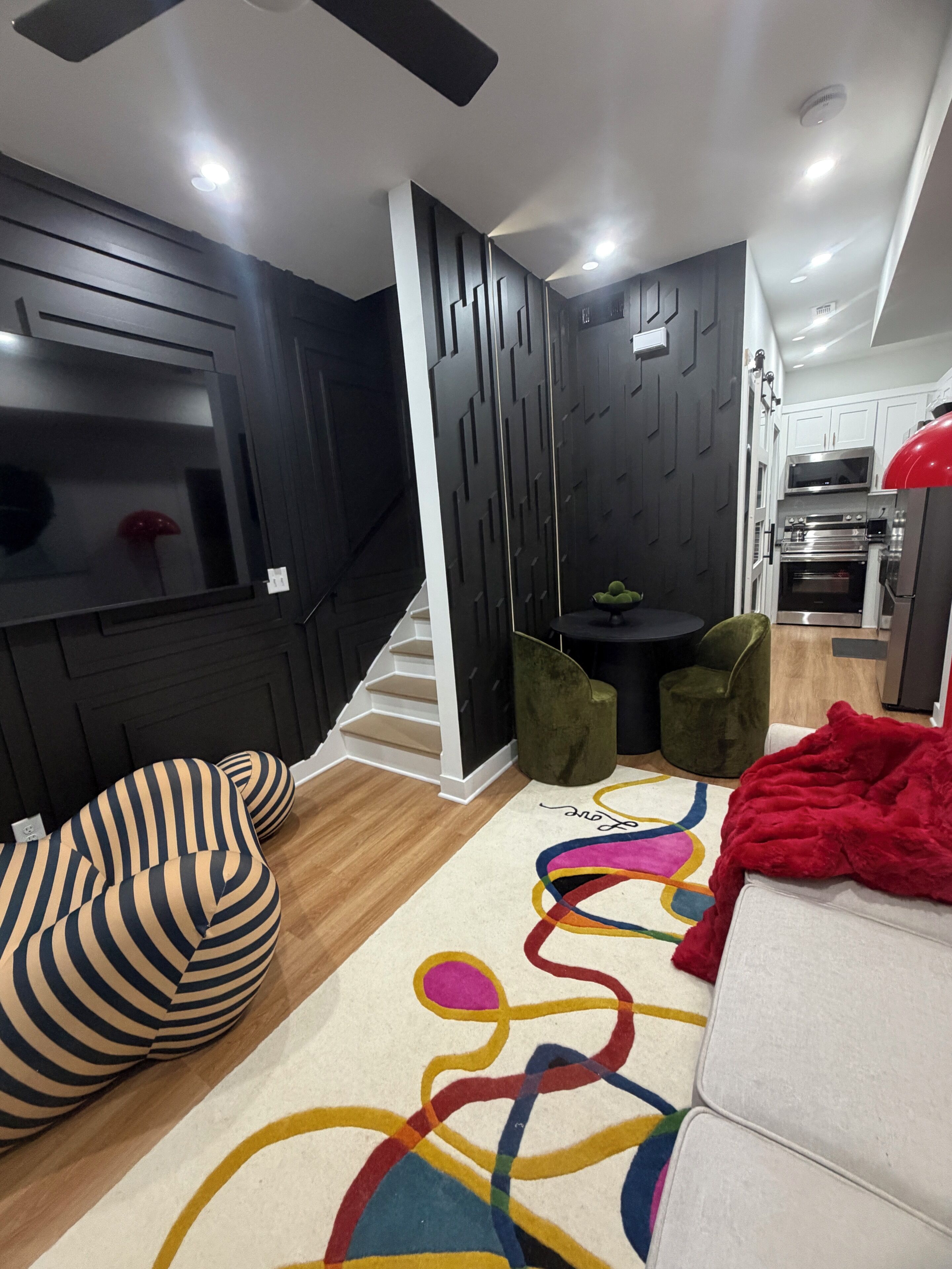 A compact living space with a sofa, a green chair, a small table, and a kitchen area with appliances.