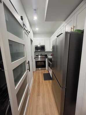 A modern kitchen with white cabinets, stainless steel appliances, and a wood floor. - Brand New Stylish Artistic Tiny Home - Minutes from Airport & Downtown (Union City)