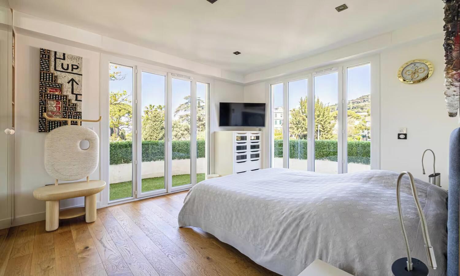 Une chambre dotée d’un grand lit, d’une télévision, d’un fauteuil et offrant une vue sur l’extérieur grâce à de grandes fenêtres.