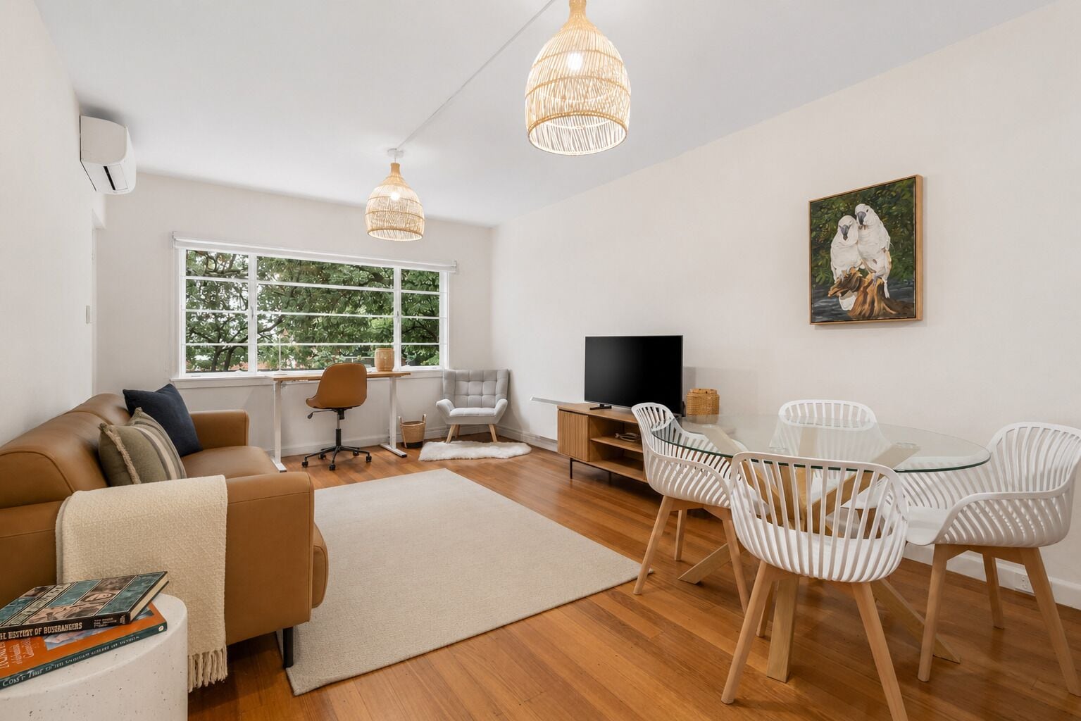 Ein modernes Wohnzimmer mit Sofa, Fernseher, Esstisch mit Stühlen und einem Bild an der Wand.