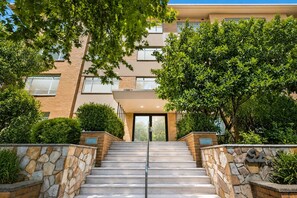 A building with a stone staircase leading to a glass door entrance, surrounded by greenery and a brick facade. - St George's Gate - Toorak by Ready Set Stay (Toorak)
