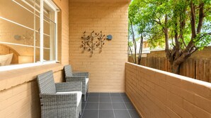 Ein schmaler Balkon mit zwei Korbstühlen, einer Ziegelwand und einem dekorativen Metallkunstwerk.
