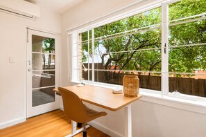 A room with a desk, chair, and a large window with a view of trees and a fence. - St George's Gate - Toorak by Ready Set Stay (Toorak)