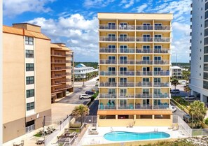 Ein mehrstöckiges Hotel mit Balkonen, einem Schwimmbad und einem Parkplatz.