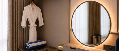 A modern bathroom with a marble countertop, a round mirror, a robe hanging on a rack, and a towel on the counter.
