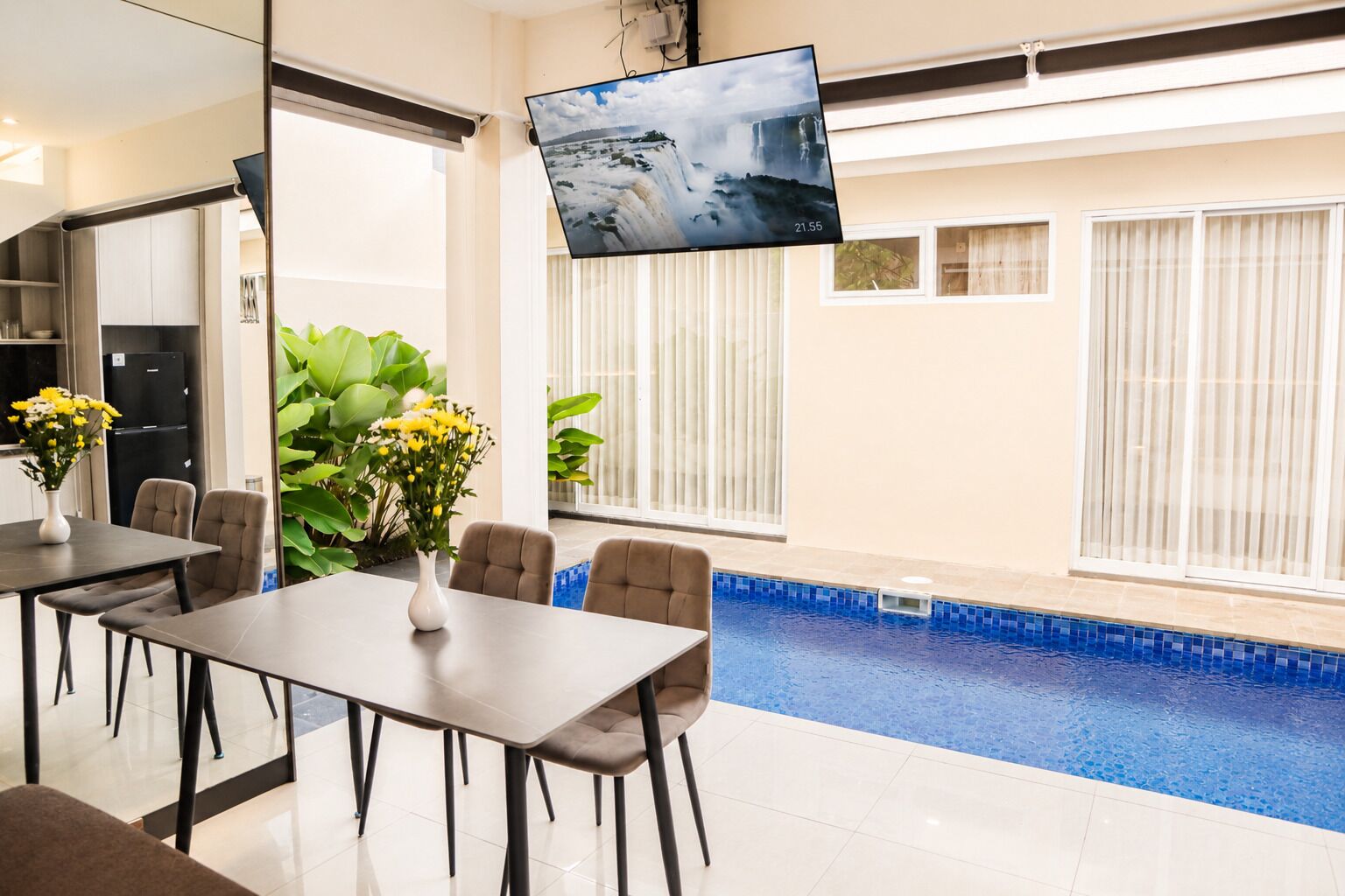Habitación de hotel moderna con zona de comedor, televisor de pantalla plana grande, piscina y ventanas amplias.