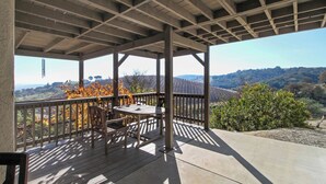 A covered outdoor patio with a table and chairs, overlooking a vineyard and hilly landscape. - Peachy Canyon Place by Avantstay Vineyard Deck Views Near Wineries (Paso Robles)