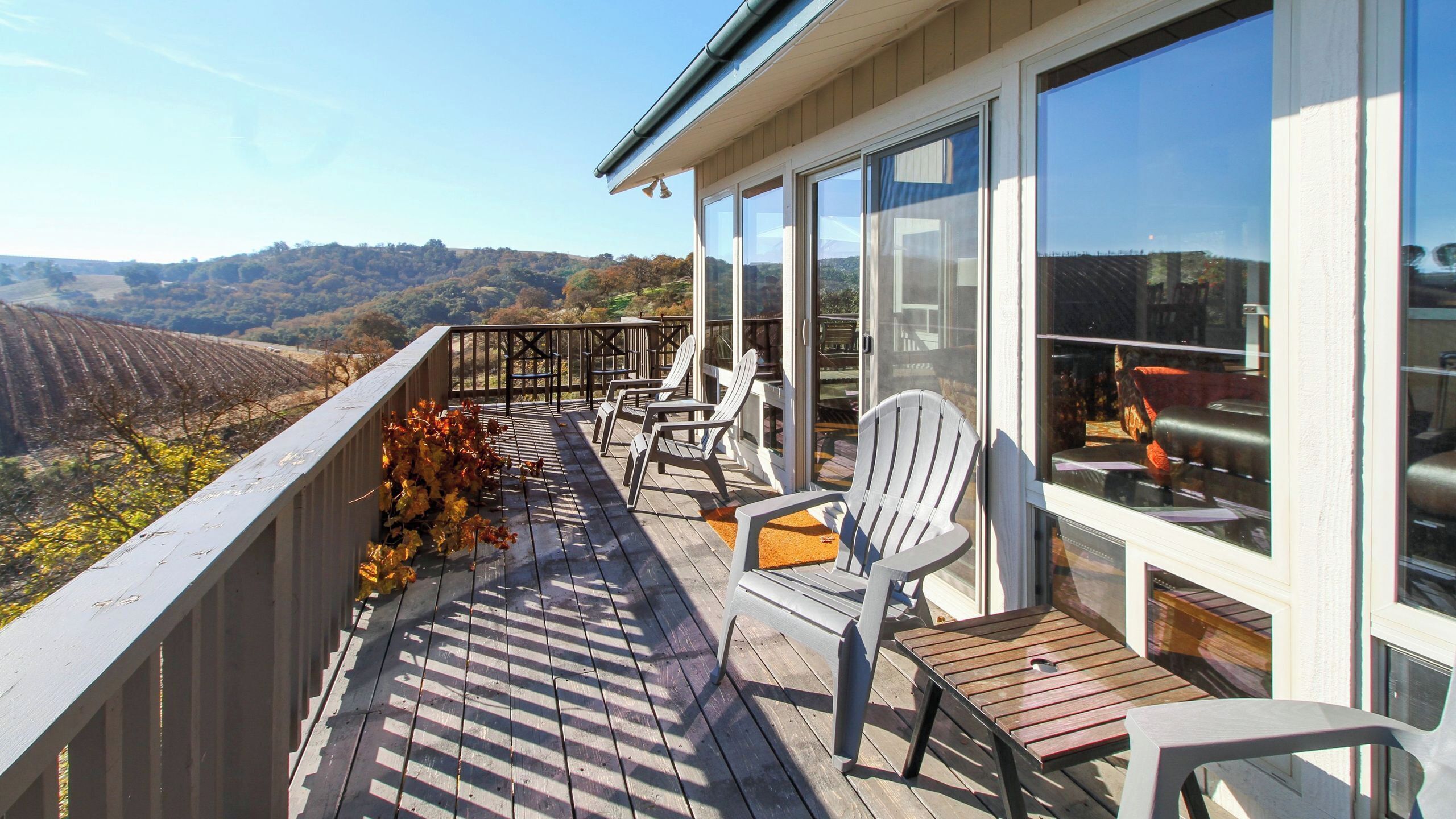 A balcony with a view of vineyards, outdoor seating, and large windows.