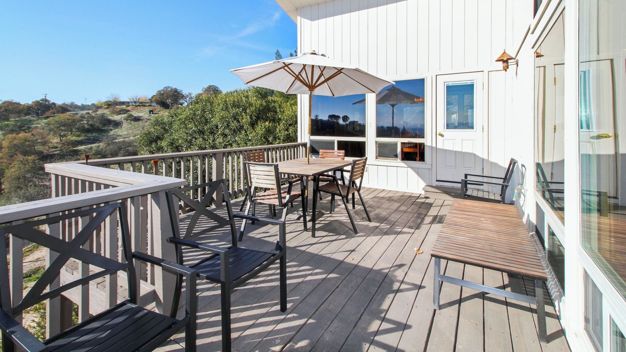 A wooden deck with outdoor furniture, including a table and chairs, and a large umbrella.