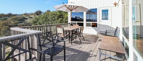 Une terrasse en bois aménagée avec du mobilier d’extérieur, notamment une table et des chaises, ainsi qu’un grand parasol.
