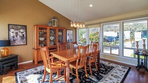 A dining area with a wooden table and chairs, a cabinet with glass doors, and a view through large windows. - Peachy Canyon Place by Avantstay Vineyard Deck Views Near Wineries (Paso Robles)