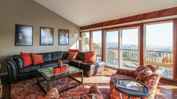 A spacious living room with a large window, a leather sofa, a coffee table, and a patterned rug. - Peachy Canyon Place by Avantstay Vineyard Deck Views Near Wineries (Paso Robles)