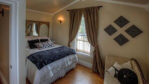 A bedroom with a large bed, a window with curtains, a bedside table, and decorative wall art. - Bliss House by Avantstay Victorian Charm + Gazebo Yard + Corn Hole Walk to Dining + Park (Paso Robles)