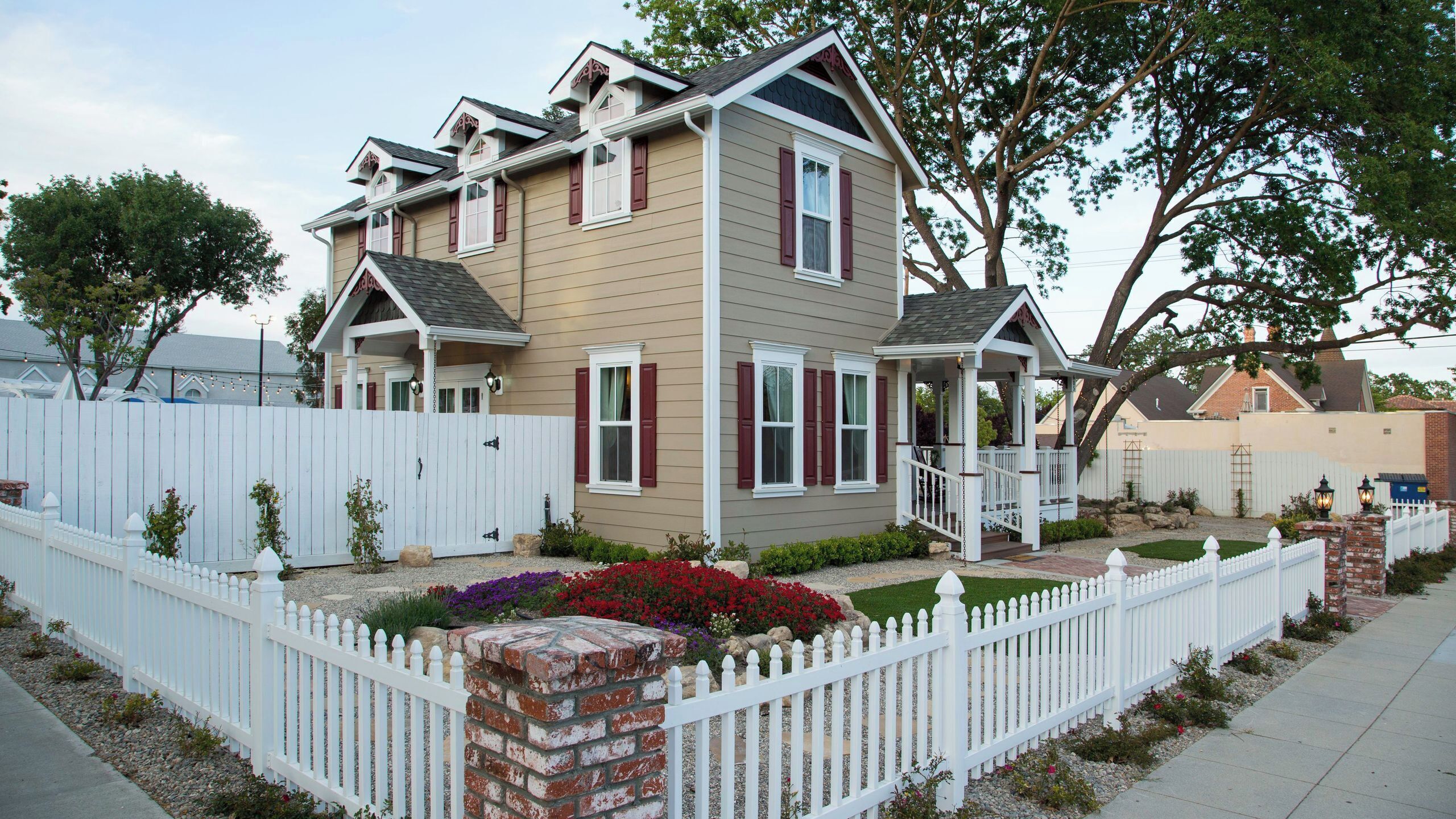 A two-story house with a front porch, a brick column, and a white picket fence.