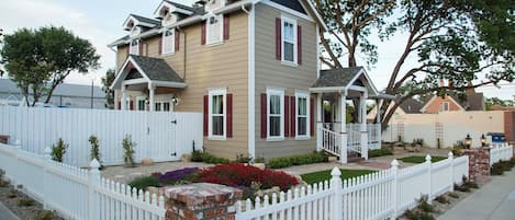 A two-story house with a front porch, a brick column, and a white picket fence.