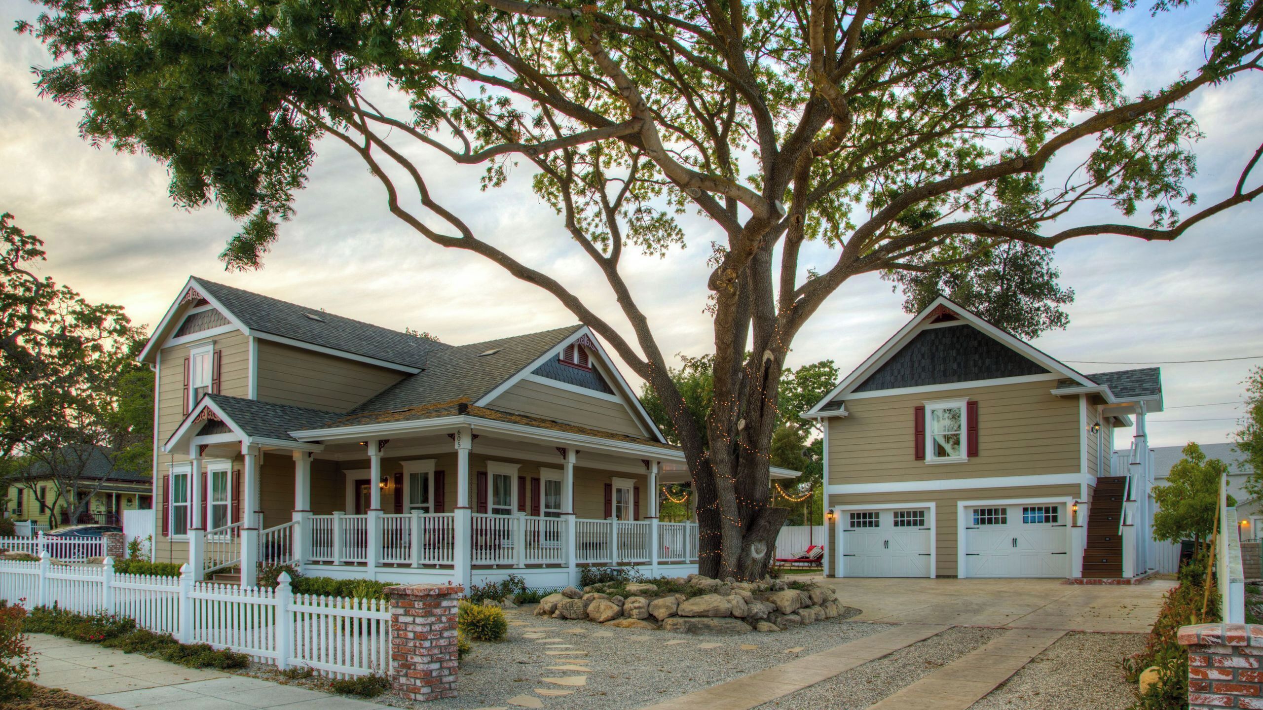 A two-story house with a porch, a garage, and a large tree in front.