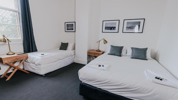 A hotel room with two single beds, a desk, and a window with curtains. - Holmesville Hotel (Holmesville)