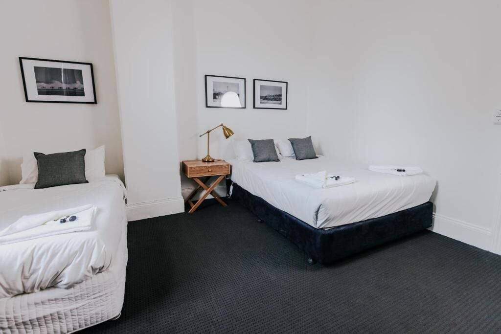 Ein Hotelzimmer mit zwei Betten, einem Nachttisch, einer Lampe und gerahmten Bildern an der Wand.