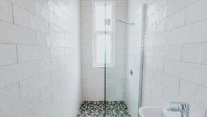 A bathroom with white tiled walls, a shower with a glass door, and a sink with a modern faucet. - Holmesville Hotel (Holmesville)