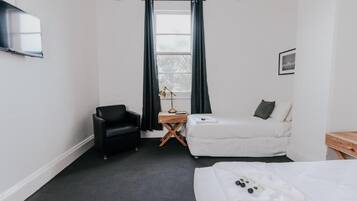 Quarto de hotel com cama, cadeira, mesa pequena, luminária e janela com cortinas.