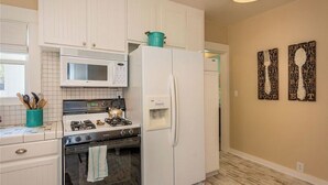 A kitchen with white cabinets, a microwave, a stove, and a refrigerator. There are kitchen utensils in a teal container. - The Sycamore by Avantstay Fenced Yard + BBQ Walk to Downtown Wineries (Paso Robles)