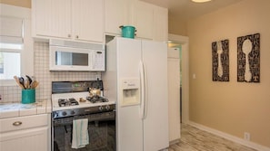 A kitchen with white cabinets, a microwave, a stove, and a refrigerator. There are kitchen utensils in a teal container. - The Sycamore by Avantstay Fenced Yard + BBQ Walk to Downtown Wineries (Paso Robles)