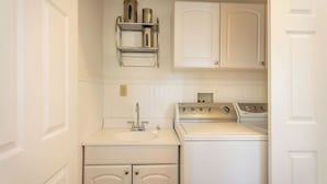 A compact laundry room with a washing machine, a sink, and a shelf above the sink. - The Sycamore by Avantstay Fenced Yard + BBQ Walk to Downtown Wineries (Paso Robles)