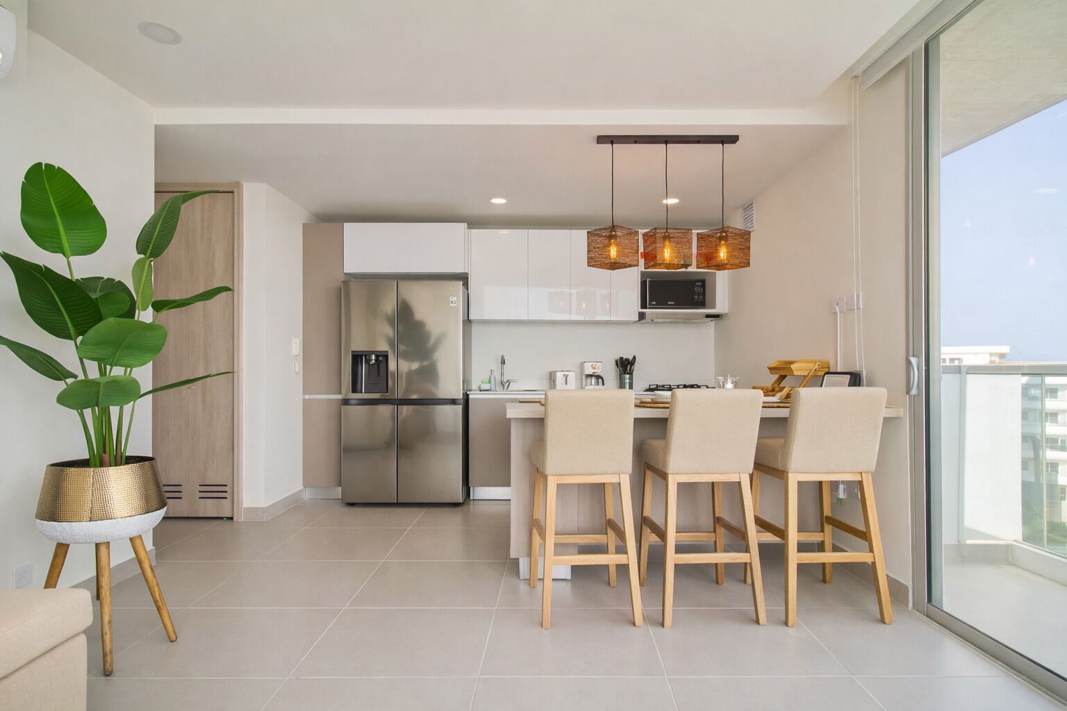 Una cocina moderna con un refrigerador de acero inoxidable, una zona de comedor con mesa y sillas, y un ventanal con vistas.